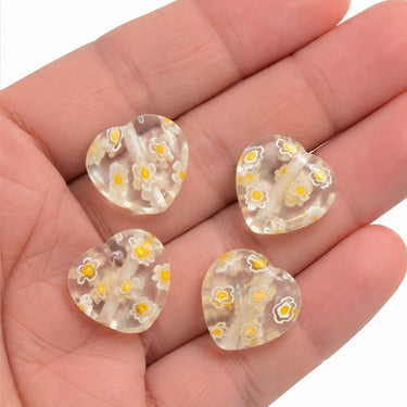 Fire klare 10 mm millefiori glashjerter med gule blomster vist i hånden